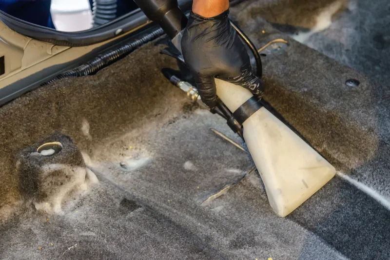 Gloved hand holding an extractor wand cleaning a carpeted car floor